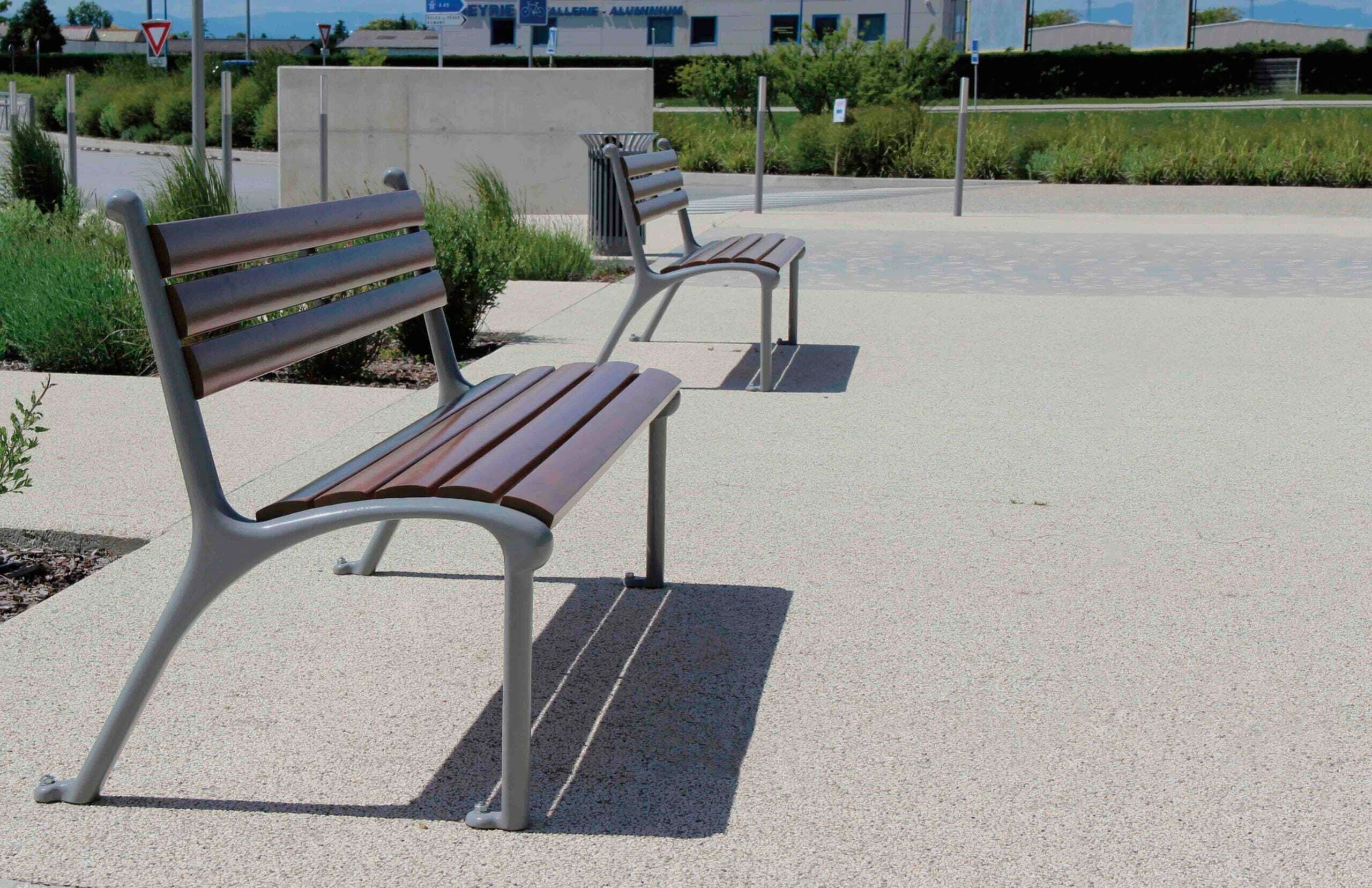Two park benches with wooden slats and grey cast frames on a paved plaza